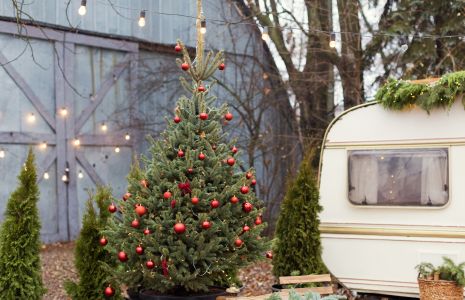Vintage old travel trailer with Christmas decorations, Christmas tree, chair and Christmas lights. Cozy home, camping before Christmas holidays.
